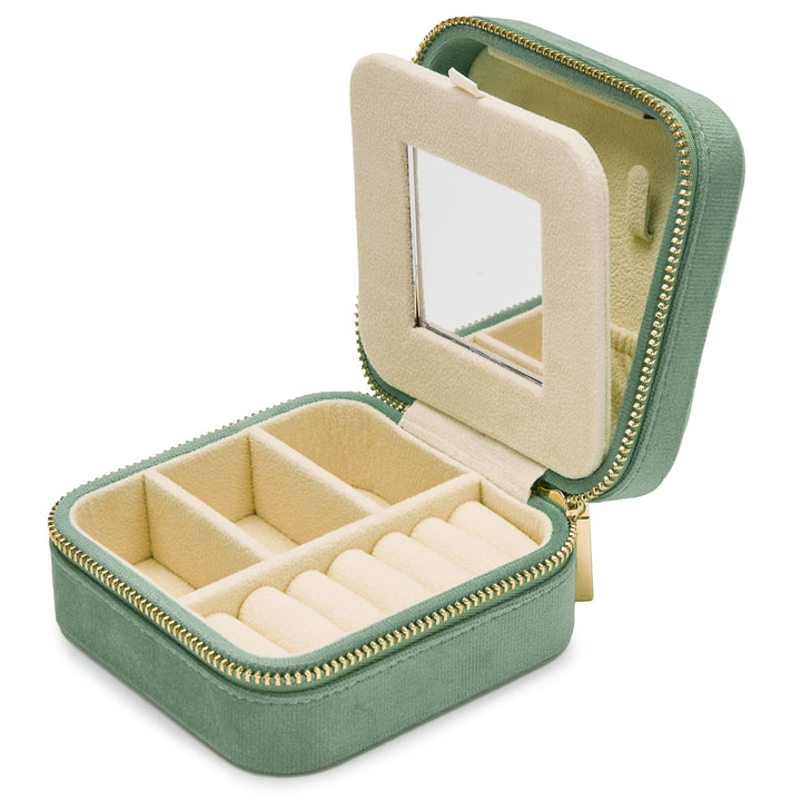 A small, square, velvet-covered jewelry box with a zippered closure is open, revealing a beige interior. The travel-friendly interior has compartments for rings and other jewelry, and the lid features a small mirror. The Luxurious French Green Velvet Travel Jewellery Box by SoCases is perfect for organizing your accessories on the go.