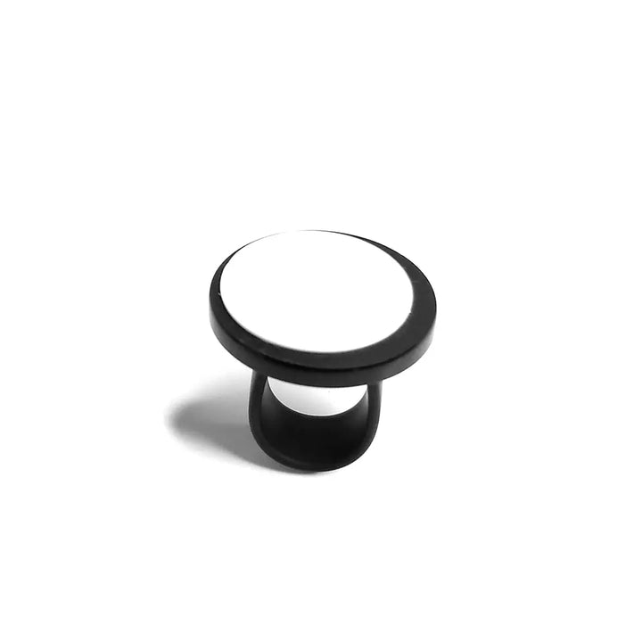 An Amy Ring from Alex + Svet with a white top is shown against a plain white background. The Amy Ring is in its expanded position, displaying its circular design and shadow cast underneath, reminiscent of the elegance found in handcrafted jewelry from a Paris studio.