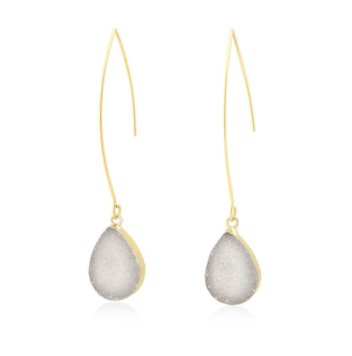 The Eira Earrings by Aria V are gold drop earrings featuring a long, thin hook with a teardrop-shaped, frosted, translucent pendant at the end. Handcrafted to perfection, their simple and elegant design highlights the smooth texture and delicate appearance of the AB white Druze quartz pendants.