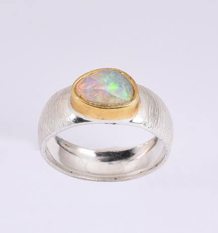 A silver ring with a silver etched band and an oval-shaped Ethiopian Opal set in a gold bezel setting. The opal displays a vibrant array of colors, primarily green and blue. The Ethiopian Opal Silver & Gold Ring by Watermelon Tropical is shown against a plain, white background.