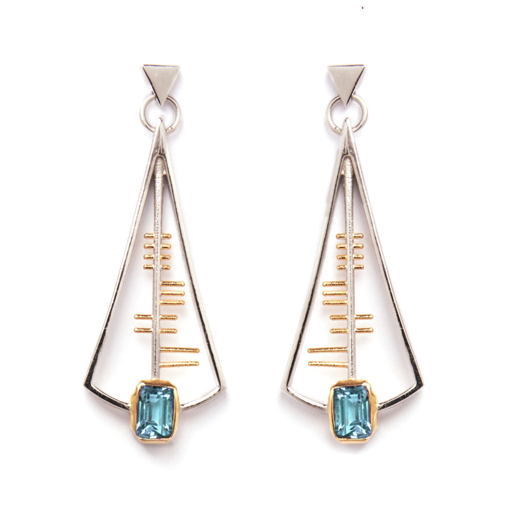 The Adeline Earrings by Gallardo & Blaine Designs feature a geometric, Art Deco-inspired design with a triangular sterling silver frame accented with gold and centered around a striking rectangular blue gemstone at the base. These earrings showcase a sleek, modern aesthetic with minimalist lines and shapes.