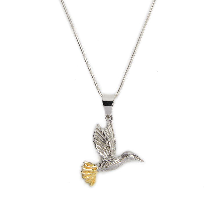 A Wildlife Pendant - Bird In Flight With Chain from Gallardo & Blaine Designs features a bird in flight pendant, capturing a hummingbird mid-flight. The bird's tail feathers are accented with a touch of gold. The sleek, thin silver chain enhances the elegant and delicate design of the pendant.