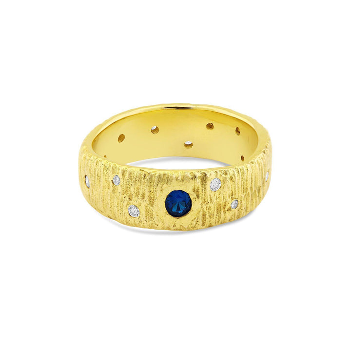 A textured 9 ct yellow gold ring featuring a central real sapphire is surrounded by six small white diamonds, evenly spaced around the ring's circumference. The inner band is smooth with small, evenly spaced holes. The Etta Ring with Sapphire & Diamonds from Gallardo & Blaine Designs.