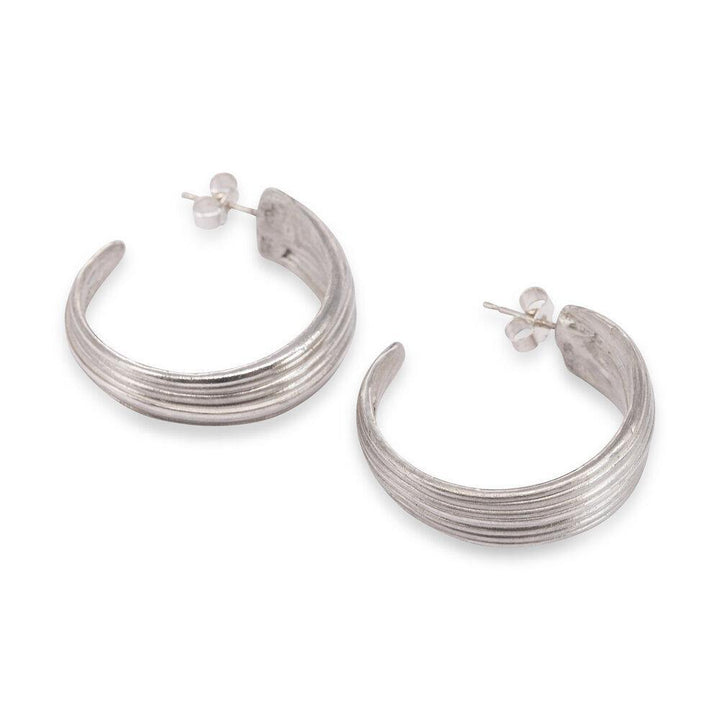 A pair of exquisite Abbie Dixon Mitsuro Hoop Earrings in sterling silver, featuring a crescent-shaped hoop design with a textured, ribbed finish. These lost wax method earrings have post backs and are displayed side by side on a pristine white background.