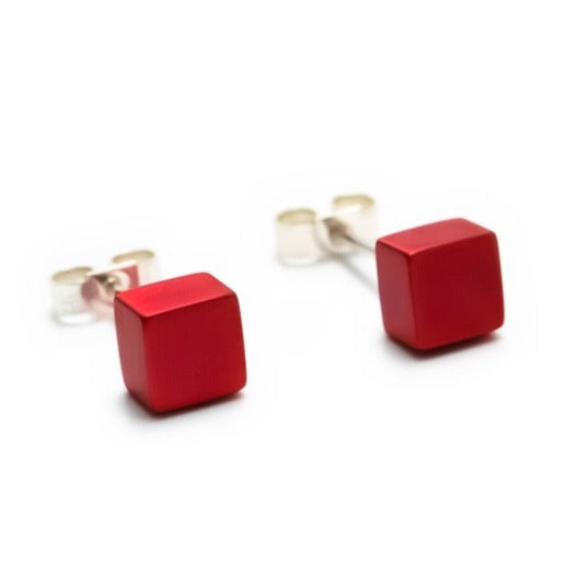 A pair of Small Cube Stud Earrings by Filip Vanas featuring small, square red cubes crafted from anodized aluminium. The earrings have sterling silver-toned posts and clear backings, set against a white background.