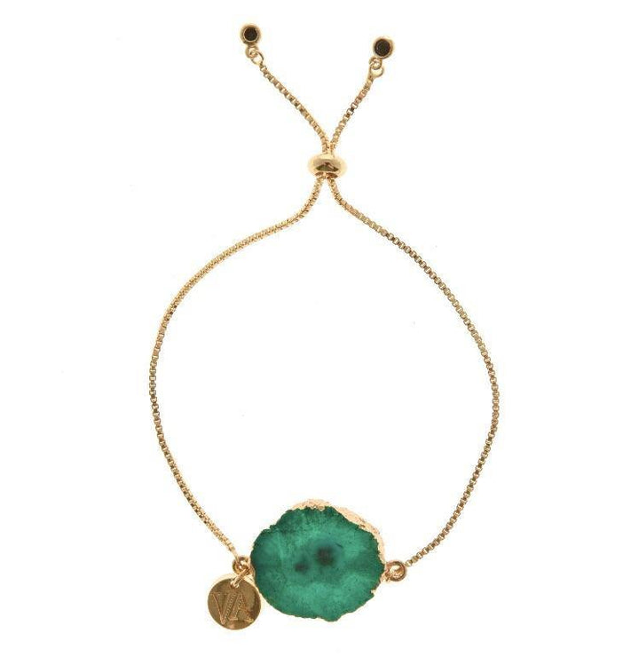 The Holly Bracelet by Aria V is a gold-plated bracelet with an adjustable clasp that features a green, semi-precious stone with natural, irregular edges as its centerpiece. Handmade in Dublin, it includes a small round gold charm engraved with a "V" next to the stone.