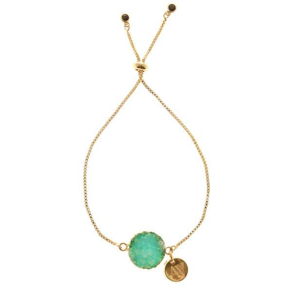 Gold-plated Ivy Bracelet with an adjustable chain, featuring a large mint green Druze stone pendant and a smaller round gold charm. The Druze stone is set in a gold frame, and the charm is engraved with a design. The adjustable ends have small round gold beads. This is part of the Aria V collection.