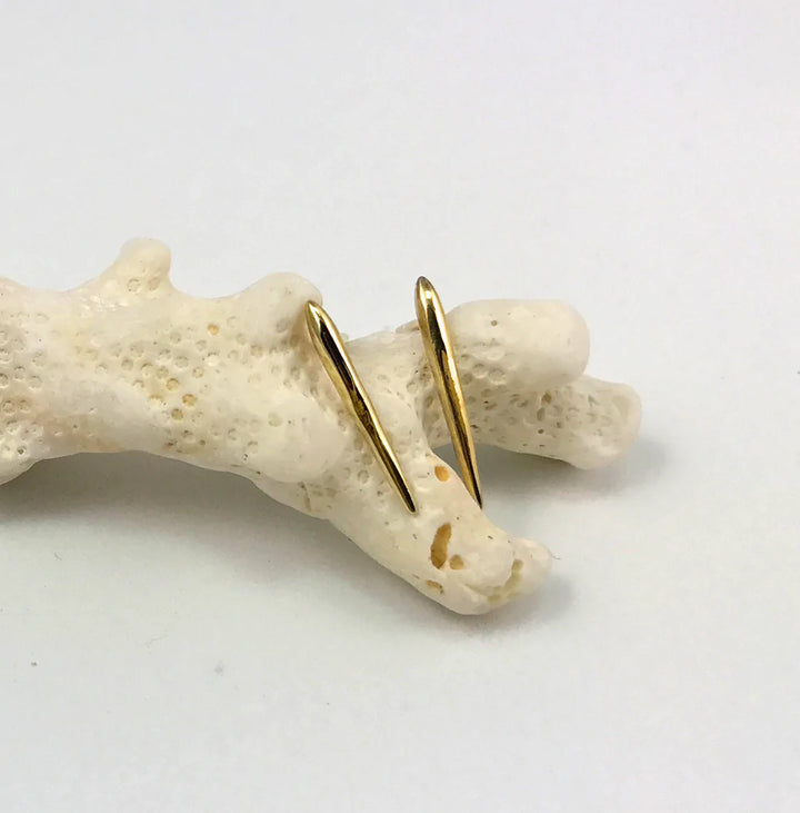 Jennifer Kinnear’s Sea Urchin Spine Earrings - Gold in various sizes, featuring a sleek gold-plated silver design, are displayed on light-colored coral with a plain white background.