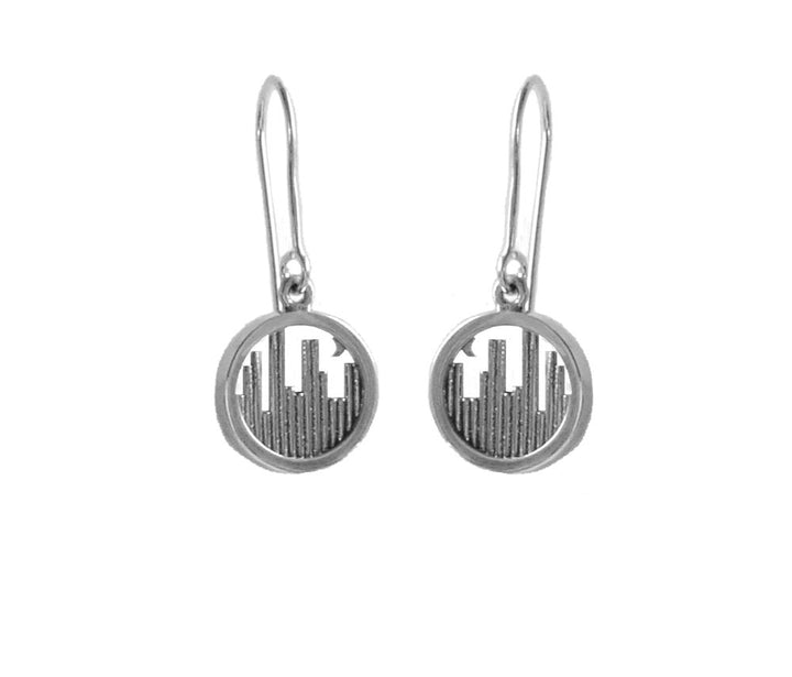 A pair of Miriam Wade Skyline Drop Earrings Silver with oval-shaped charms, each featuring a city skyline cutout design. The earrings have thin hooks for wearing. The skyline pattern inside the oval charms creates an urban and modern aesthetic, with an Irish Hallmark guaranteeing their quality.