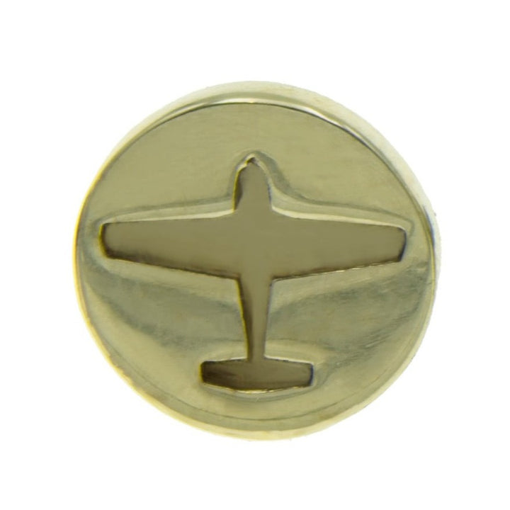 A gold-colored circular brass pin featuring an embossed silhouette of an airplane in the center. The Plane Lapel Pin by Millett Wade boasts a polished, reflective surface, making it a standout plane lapel pin.