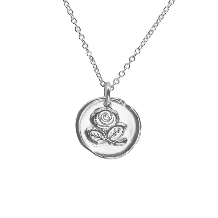 A delicate silver necklace with a round pendant. The pendant, a sterling silver disc, features an embossed design of a blooming Irish Rose with leaves. The chain is made of simple interlocking links. This piece serves as a timeless symbol of love and elegance. Introducing the Irish Rose Necklace Silver by Andrea Mears Jewellery.