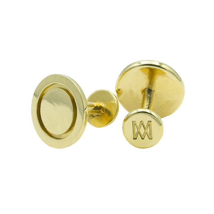 A pair of Round Cufflinks by Millett Wade with a round design. One cufflink has a simple circular pattern, while the other features an engraved logo with a stylized "W" on the back. Hand-finished from solid brass, they boast a polished, shiny finish.