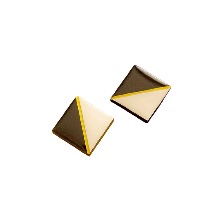 The Tetra Stud Earrings by Naoi are a pair of square-shaped, hand-painted wooden stud earrings with a modern design. Each earring is divided diagonally into two triangles: one half dark brown and the other half white, separated by a thin gold line. The background is white.